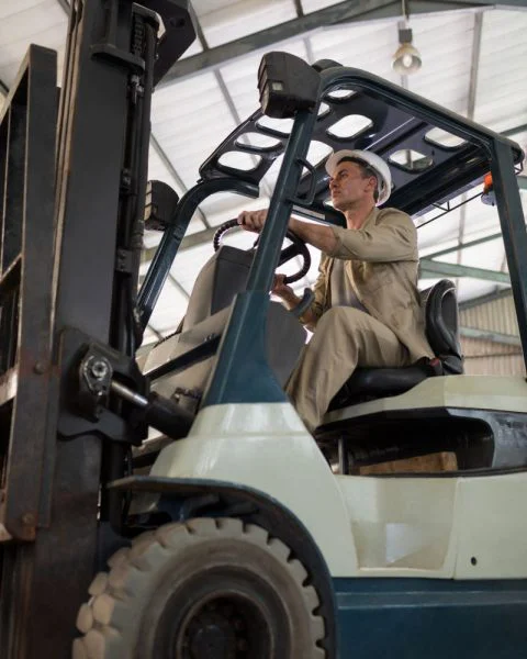 Forklift driver transporting goods with a forklift in a logistics facility.