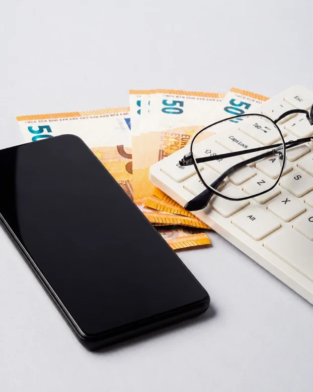 Banknoty euro, smartfon i klawiatura ilustrujące płacę minimalną w Holandii w 2023 roku