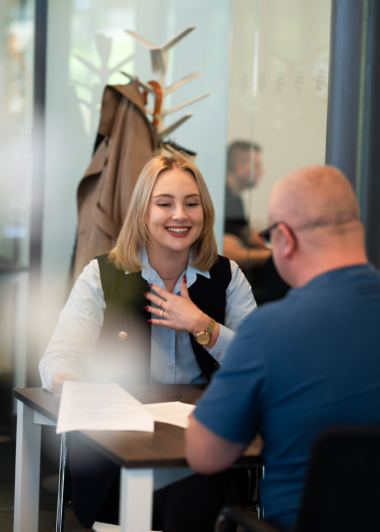 Recruiter verwelkomt een kandidaat aan zijn bureau in een licht kantoor.