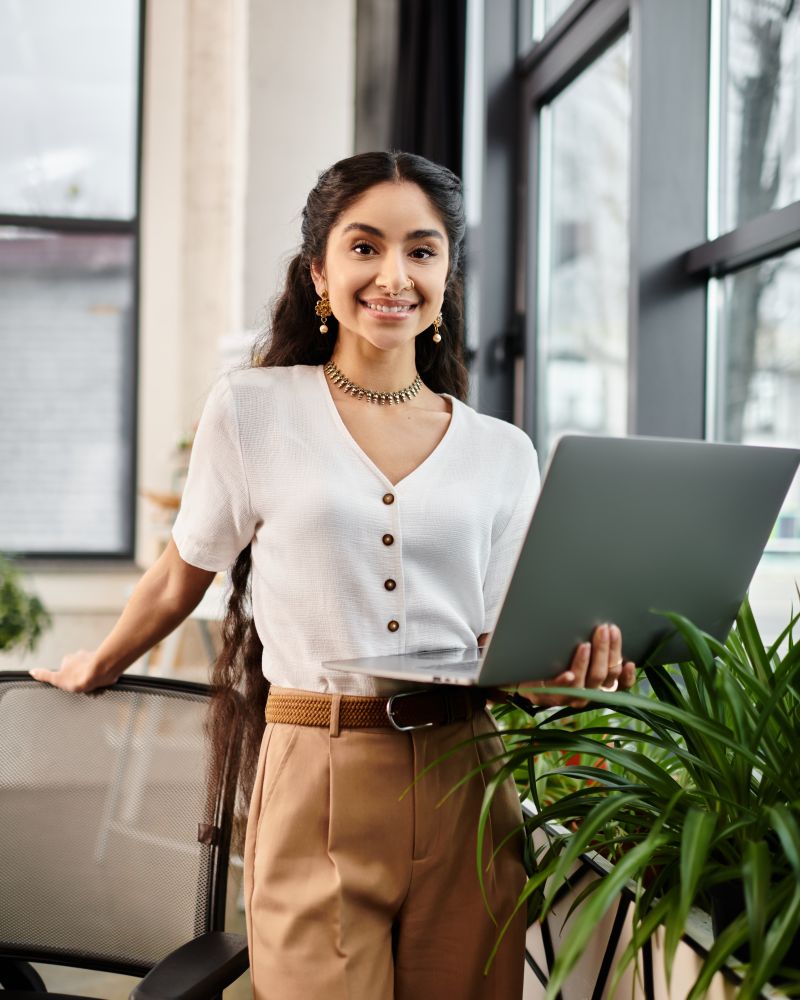 Smiling back office employee holding a laptop and looking at the camera in a bright office setting.