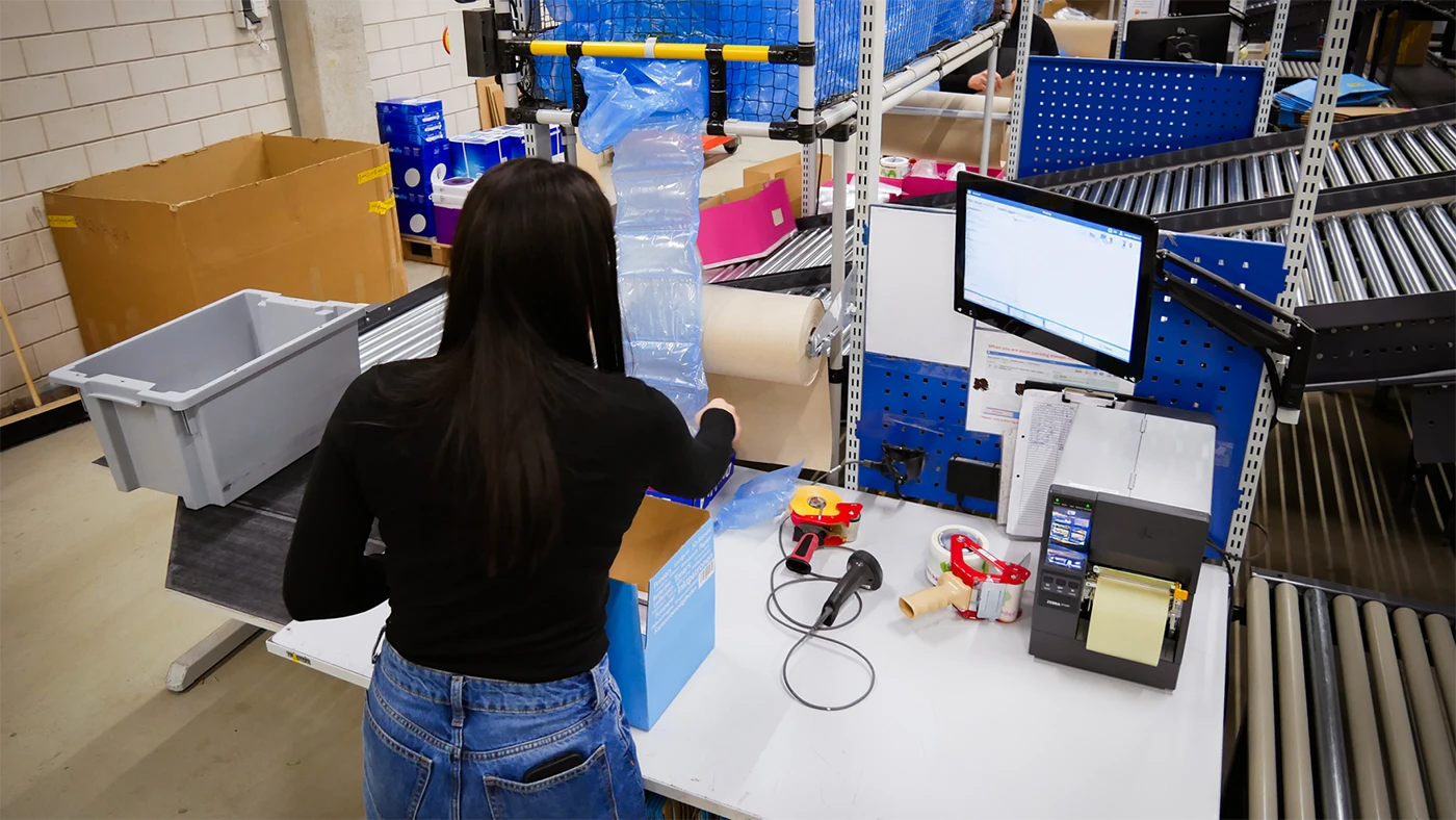 E-commerce production worker processing online orders at a packing station in a distribution center.
