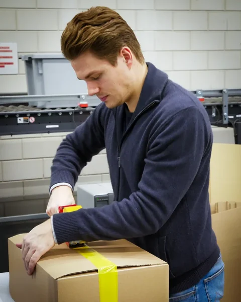 E-commerce production worker packing a customer order for shipment in a warehouse.