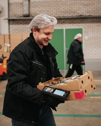 Order Picker EPT w magazynie, zbierający zamówienia i przenoszący pudełka z warzywami za pomocą ręcznego skanera.